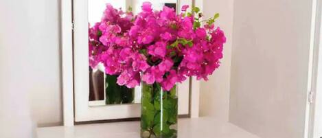 A white dresser with a mirror above it, a vase with pink flowers, and a door to the right.