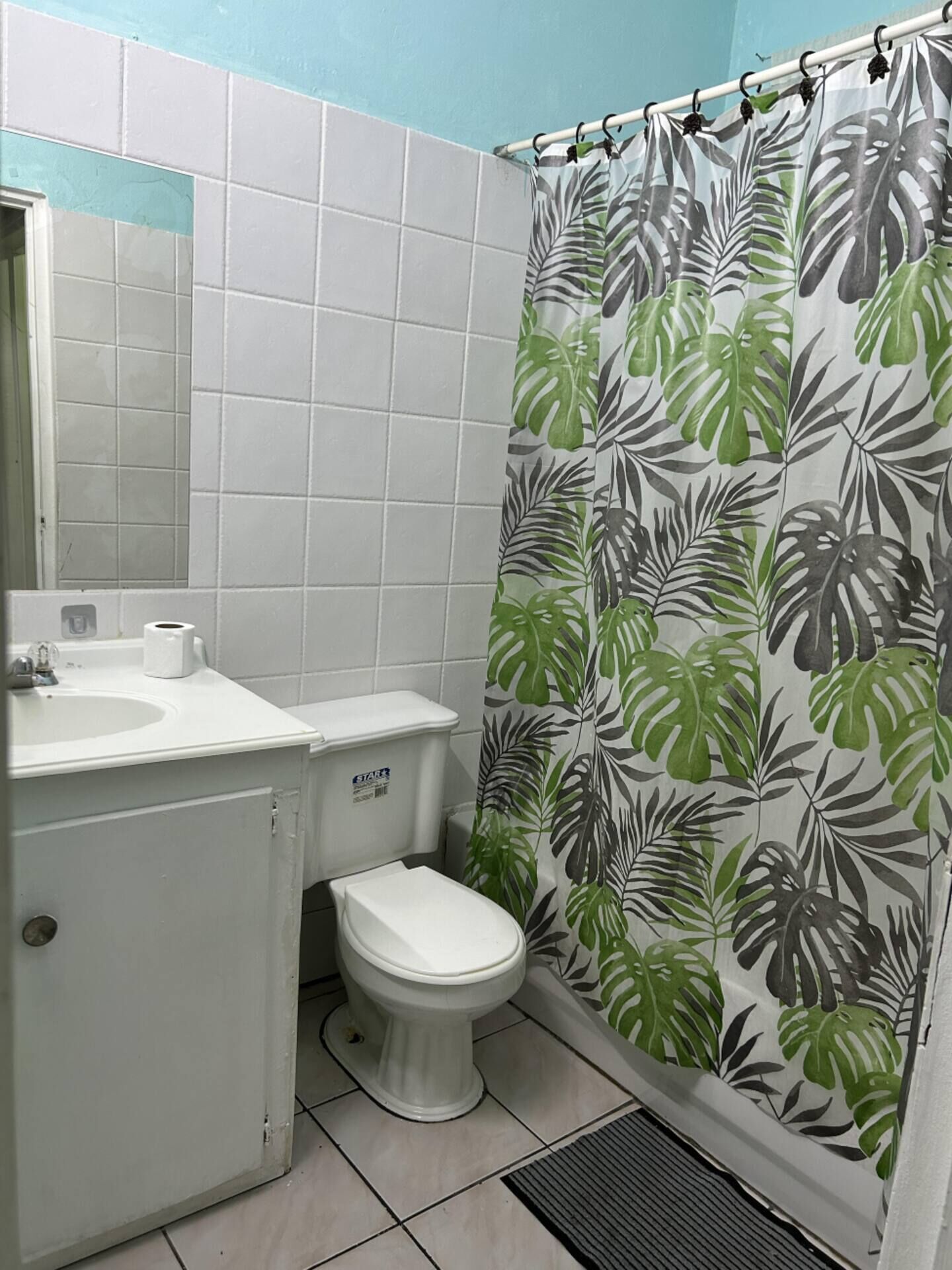 A bathroom with a toilet, sink, and shower curtain with a tropical leaf pattern.