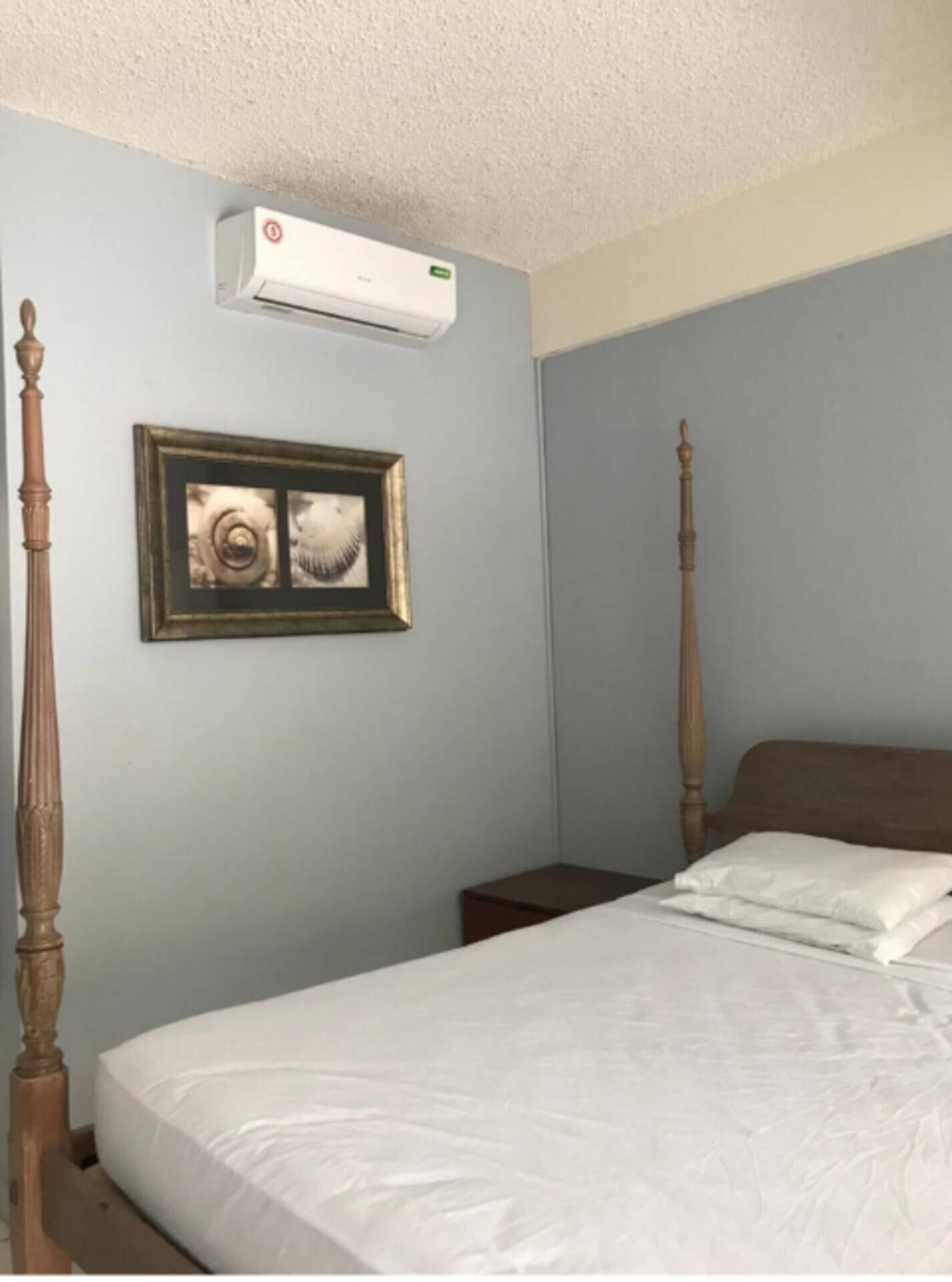 A bedroom with a bed, a nightstand, a framed picture, and an air conditioning unit on the wall.