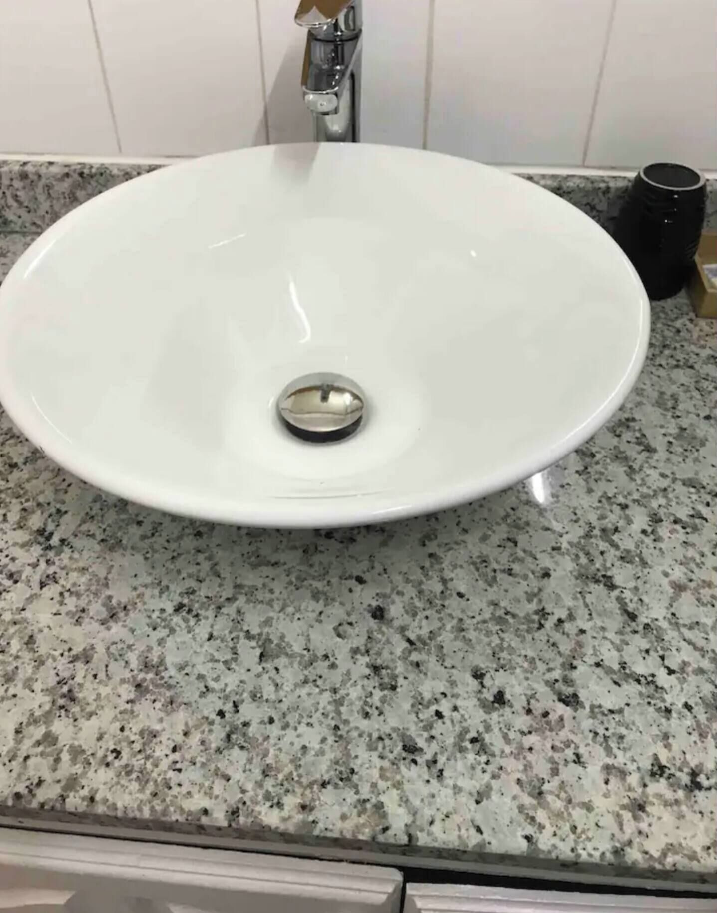 Un évier en céramique blanche, doté d’un seul drain, installé sur un plan de travail en granit à motifs.