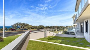 A modern building with a balcony overlooking a road and a coastal view.