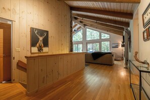 A wooden interior with a high ceiling, a fireplace, and a large window.