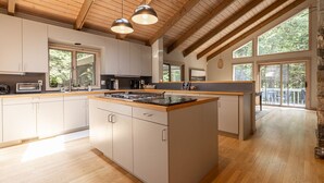 Une cuisine spacieuse avec des poutres en bois, un îlot central et de grandes fenêtres.
