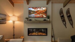 Un salon avec une cheminée, un téléviseur fixé au mur et des paires de skis accrochées au mur.