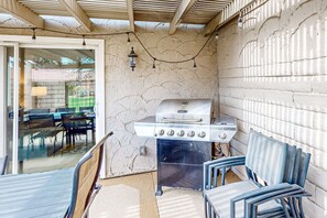 An outdoor patio with a gas grill, a covered seating area, and a sliding glass door leading to an indoor dining space. - Relaxing desert retreat with golf, gas grill, and pool (Indio)