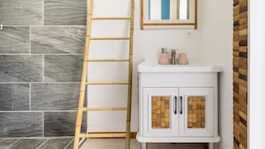 Un baño con tocador blanco, escalera de madera y pared con azulejos.