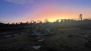 Un espacio al aire libre con césped, un atardecer de fondo, algunas sillas y una piedra con forma de corazón.