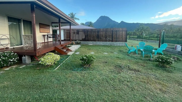 Una casa con terraza de madera, patio trasero cercado y una montaña al fondo.