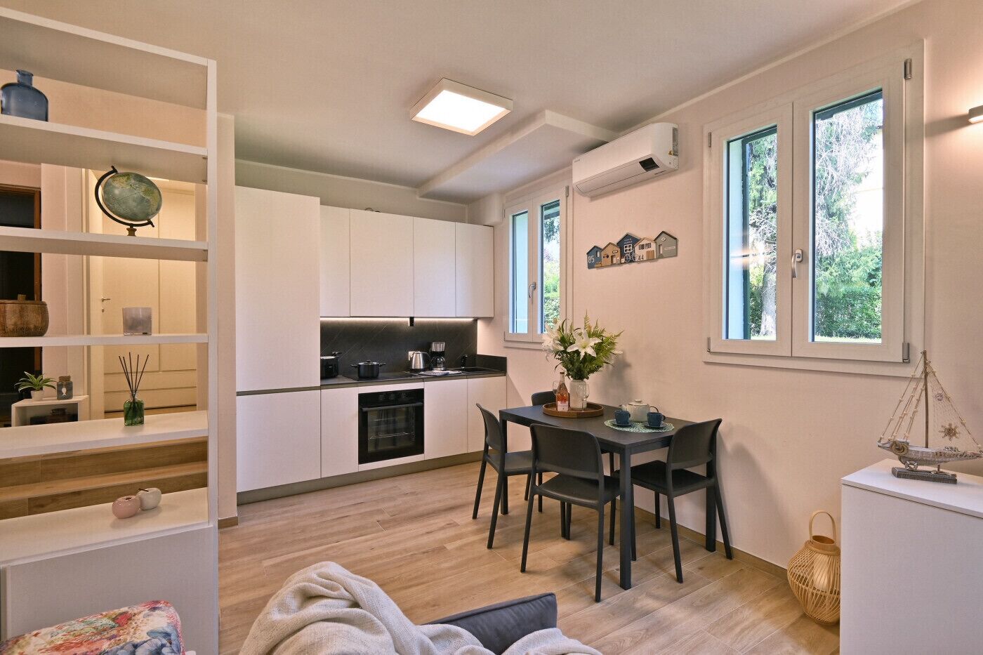 A compact kitchen with white cabinets, a dining area with a table and chairs, and a small side table with decorative items.