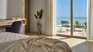 A bedroom with a bed, a desk, and a view of the ocean through a sliding glass door.