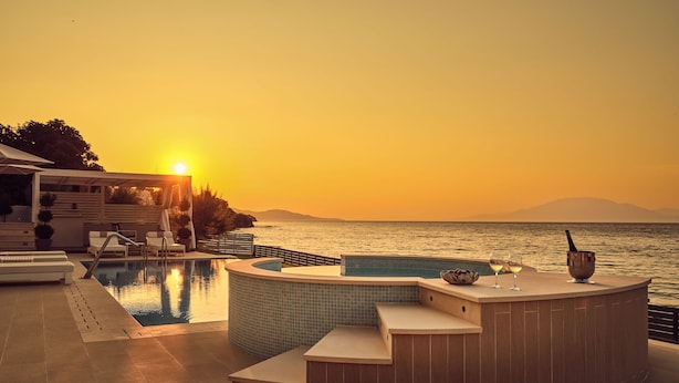 A pool area with a hot tub, lounge chairs, and a view of the sea at sunset.