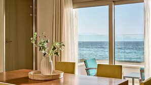 A room with a wooden table, a vase with flowers, and a view of the sea through large windows.
