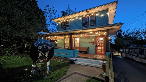 A two-story building with a porch, string lights, and a sign reading "Hostel." - Bon Paul & Sharky's Youth Hostel (Asheville)