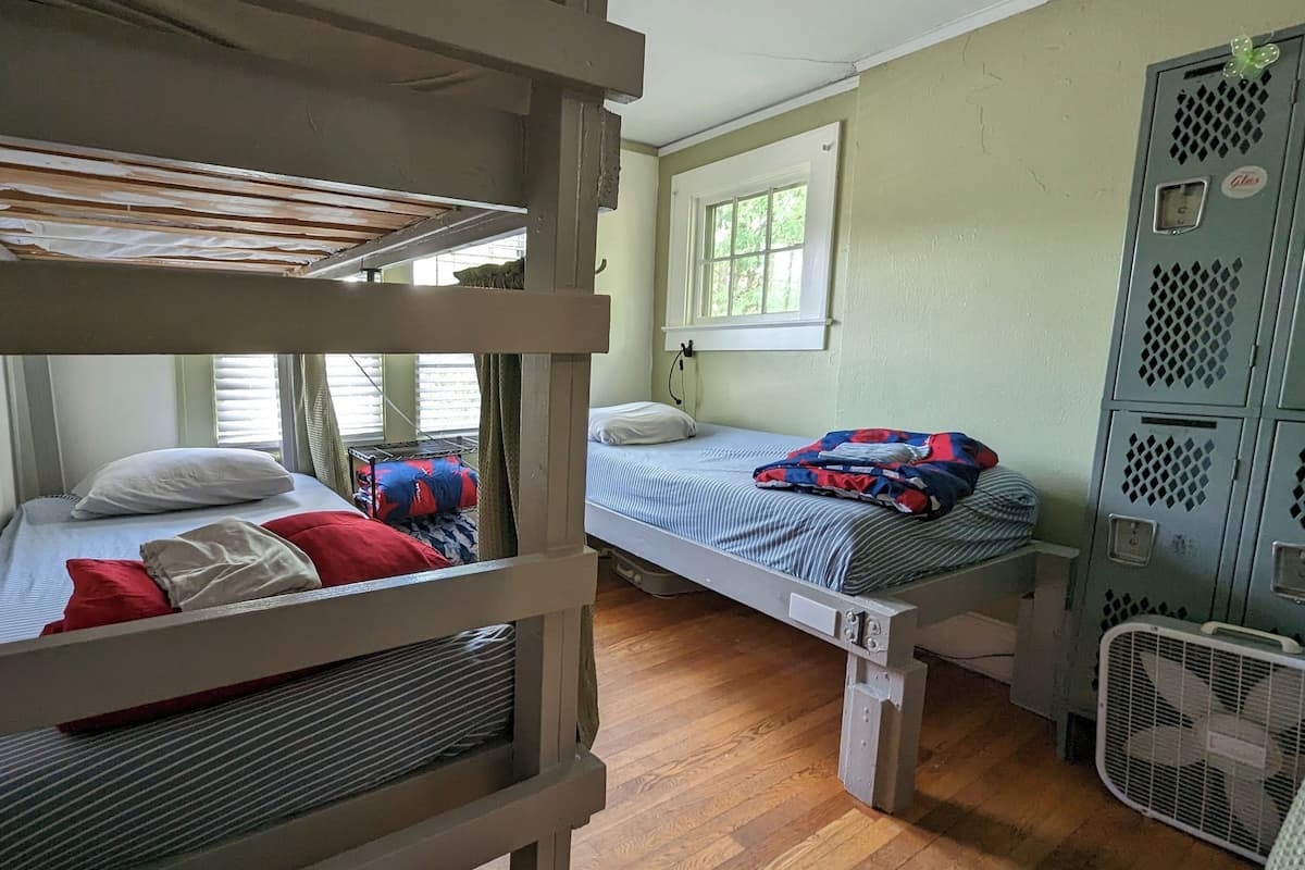 Une chambre de dortoir avec des lits superposés, une fenêtre et un ventilateur.