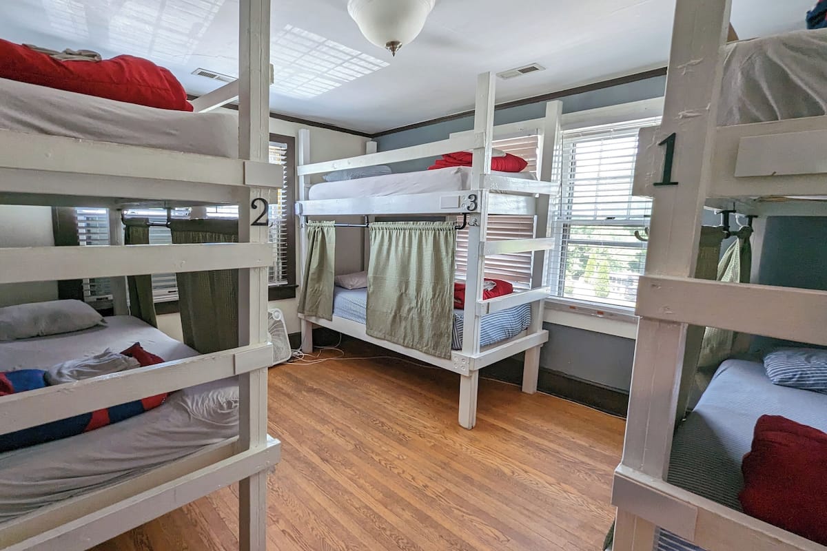 Une chambre de dortoir avec des lits superposés, un plancher en bois et un ventilateur au plafond.