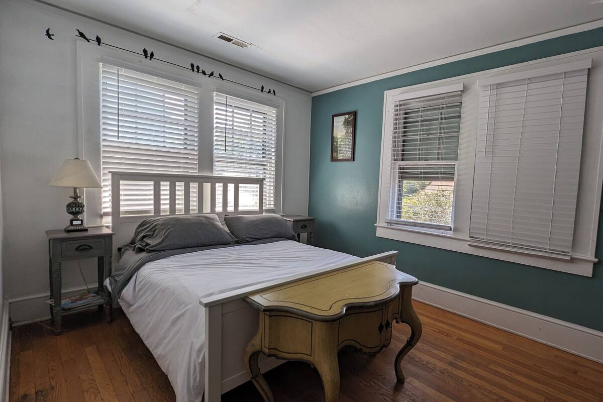 Une chambre à coucher avec un lit, un bureau et deux fenêtres équipées de stores.