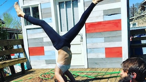 A person performing a handstand on a yoga mat in front of a wooden deck with a house in the background. - Bon Paul & Sharky's Youth Hostel (Asheville)