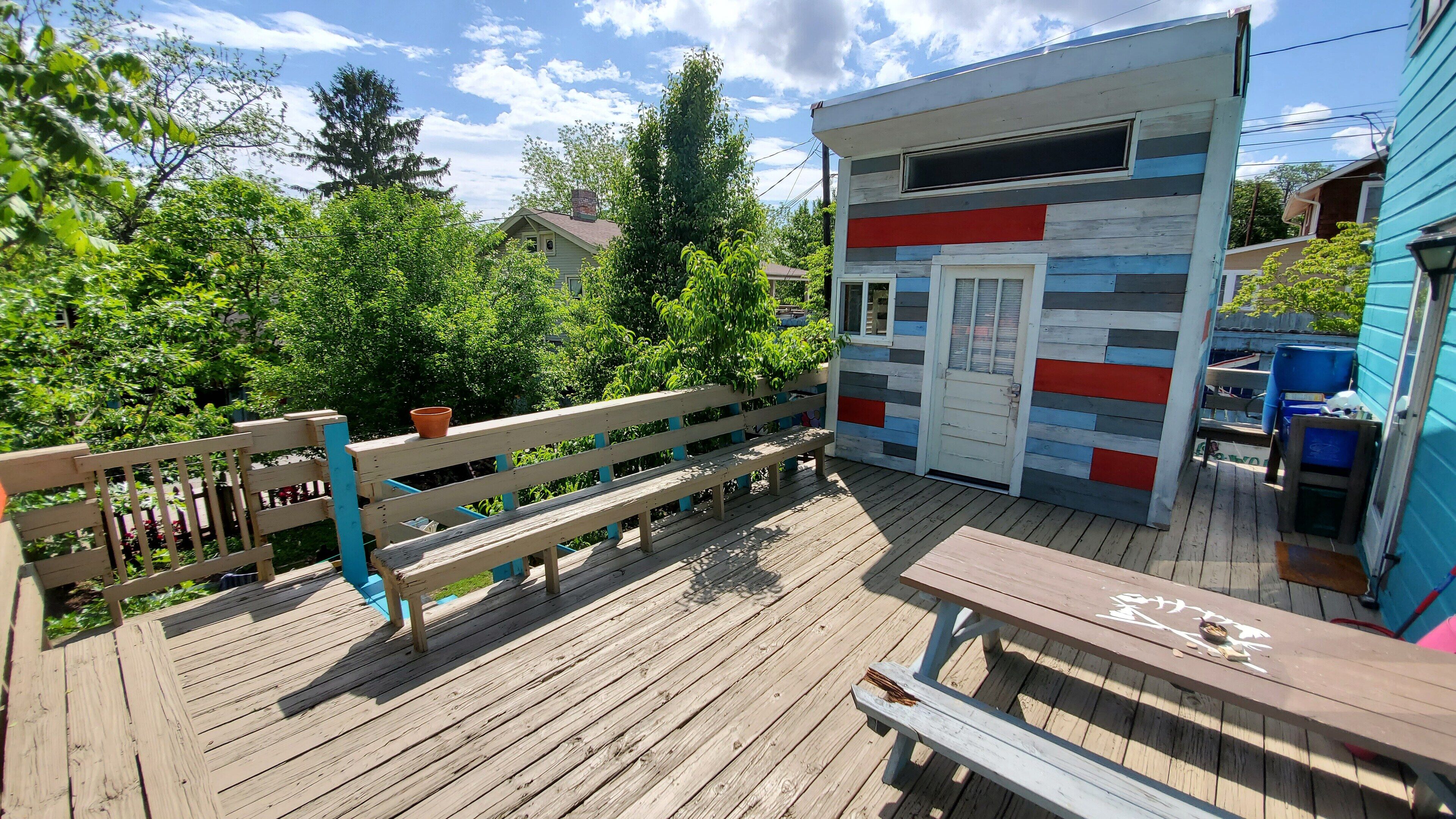 Une terrasse en bois avec un banc et un petit bâtiment à l’extérieur coloré.