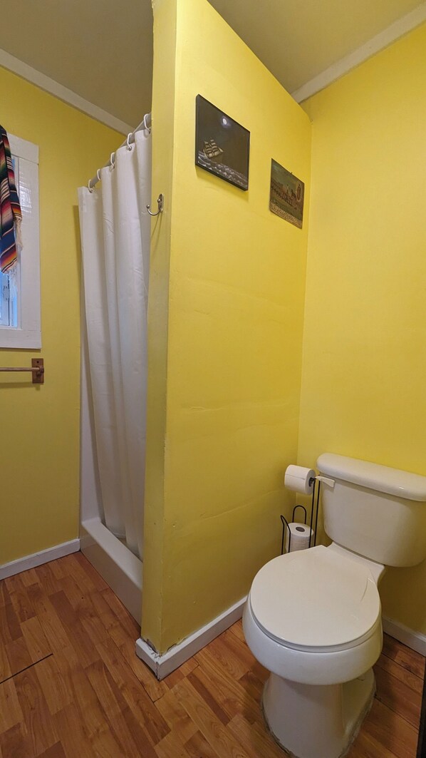 Un baño con paredes amarillas, un inodoro blanco, una cortina de ducha y dos cuadros en la pared.