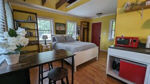 A compact room with a bed, a small table with a chair, a kitchenette with a red microwave, and a window with blinds. - Bon Paul & Sharky's Youth Hostel (Asheville)