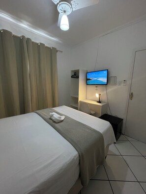 A hotel room with a bed, a desk, a television, and a ceiling fan. - Hotel Aconchegante (Jequie)