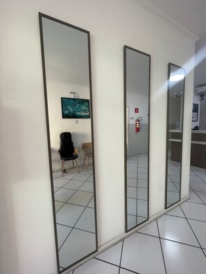 Un pasillo con tres espejos en la pared, un extintor y una silla.