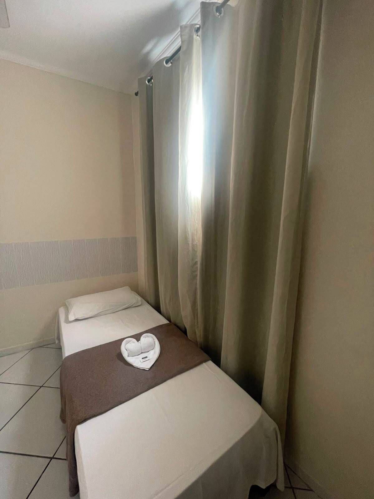 A hotel room with a bed, a brown throw blanket, and a heart-shaped towel on the bed.