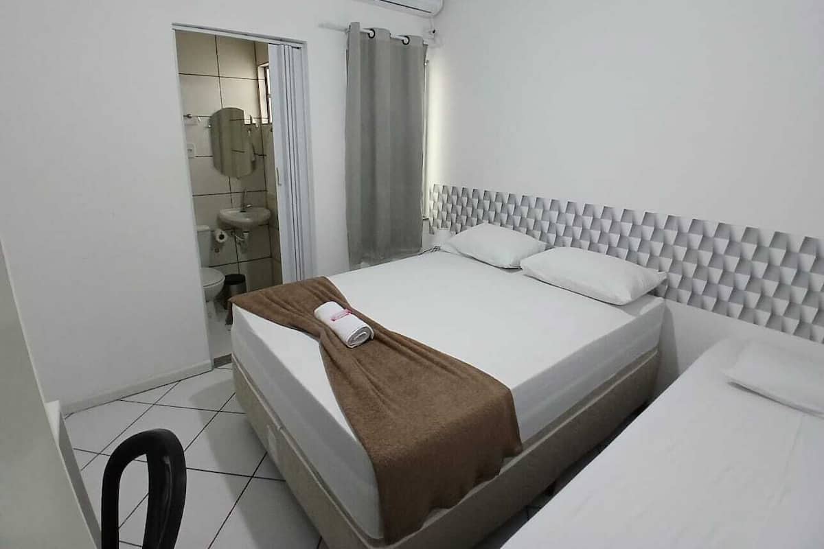 A hotel room with a bed, a bathroom with a toilet and sink, and an air conditioning unit.