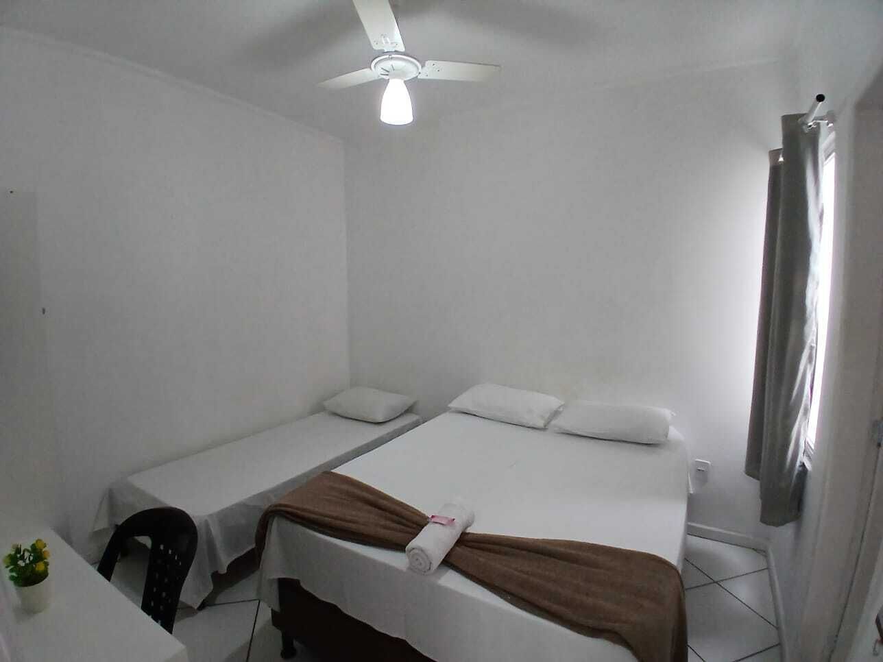 Una habitación pequeña y limpia con dos camas individuales, un ventilador de techo y una ventana con cortinas.