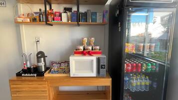 Un minibar de hotel con un refrigerador lleno de bebidas y aperitivos, un microondas y varios artículos de aseo en estantes.
