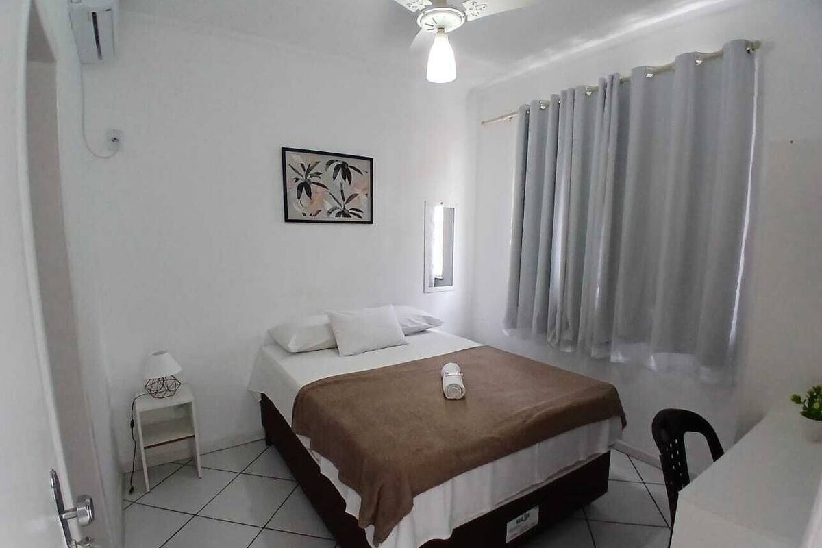 A bedroom with a bed, a nightstand, a lamp, a window with curtains, and a ceiling fan.