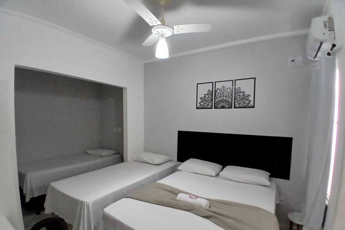 A small, compact room with two single beds, a ceiling fan, and a wall-mounted air conditioning unit.