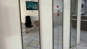 A corridor with three mirrors on the wall, a fire extinguisher, and two chairs. - Hotel Aconchegante (Jequie)