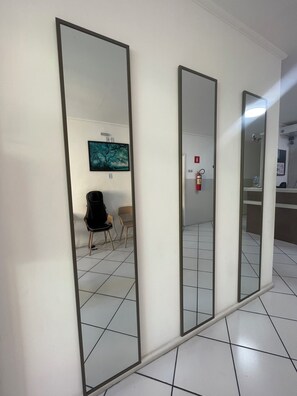 Un couloir avec trois miroirs accrochés au mur, un extincteur et deux chaises.