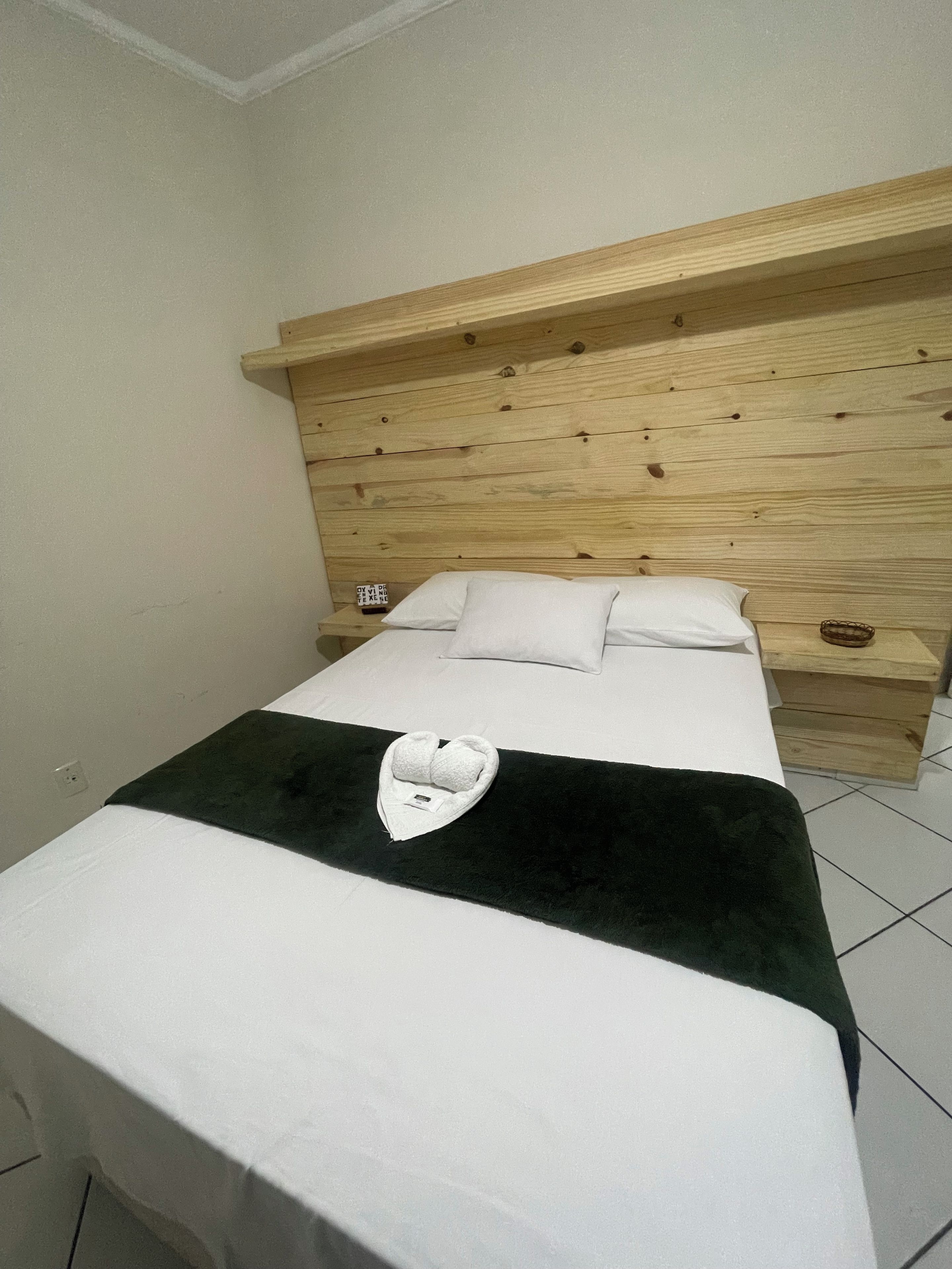 A hotel room with a wooden headboard, a bed with white bedding, and a towel on the bed.