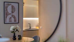 Una cocina moderna con un lavamanos integrado, una zona de comedor con una mesa redonda y sillas, y una obra de arte abstracta enmarcada en la pared.