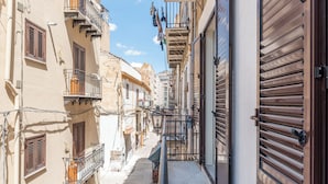 Una estrecha calle urbana flanqueada por edificios, con balcones que tienen barandillas y contraventanas.