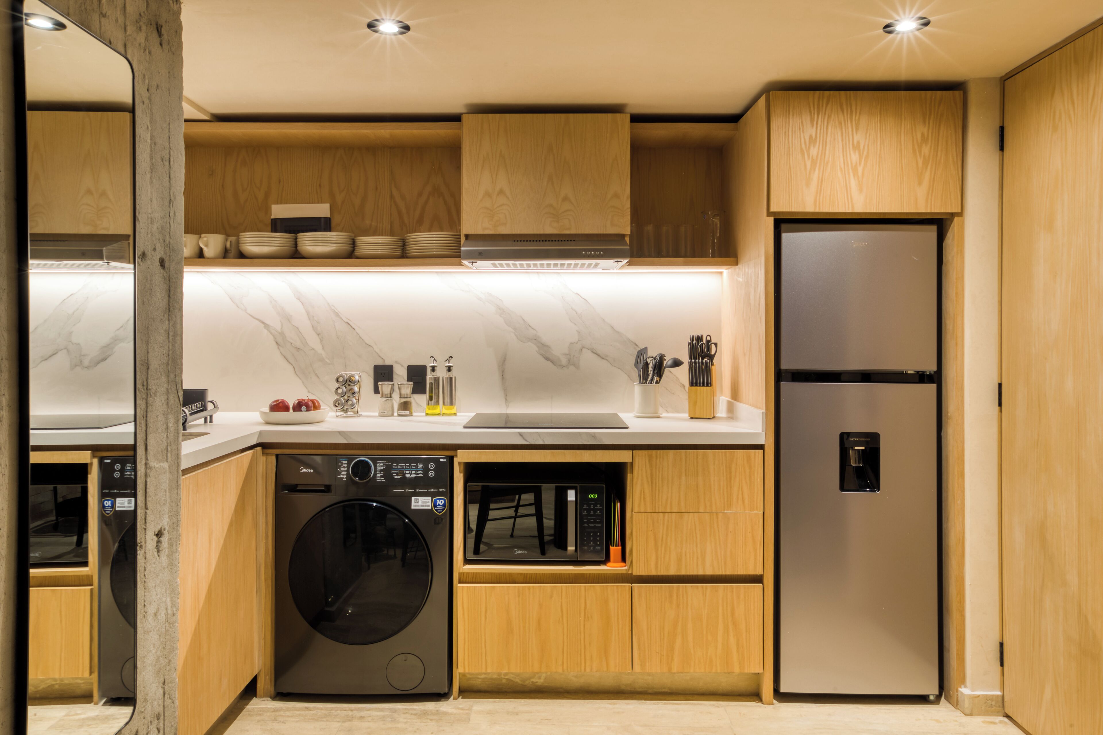 A modern kitchen with wooden cabinets, a built-in dishwasher, a stainless steel refrigerator, and a marble countertop.