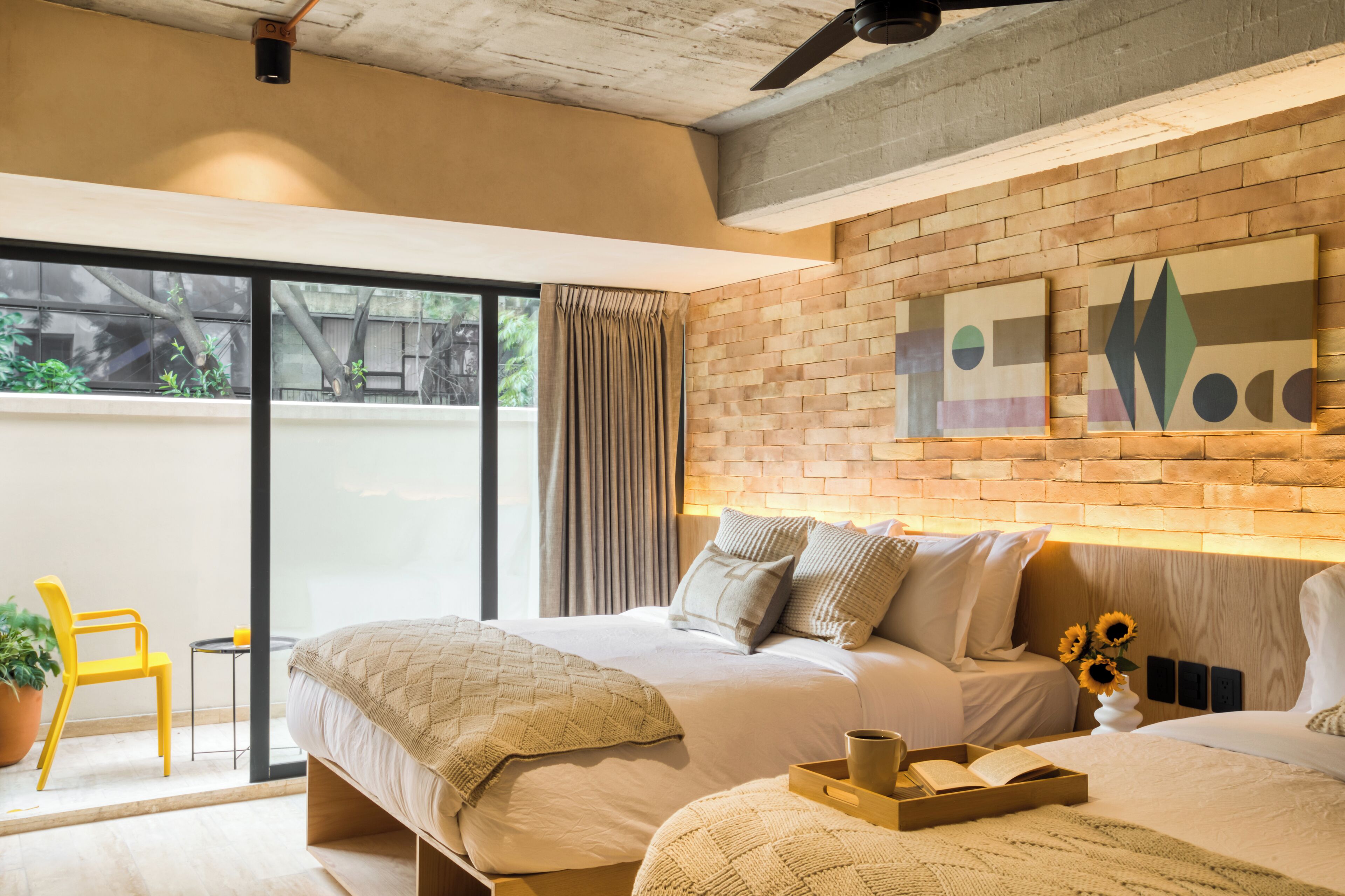 A modern bedroom with a large bed, a small bedside table, a chair, and a view of the outdoors through a sliding door.