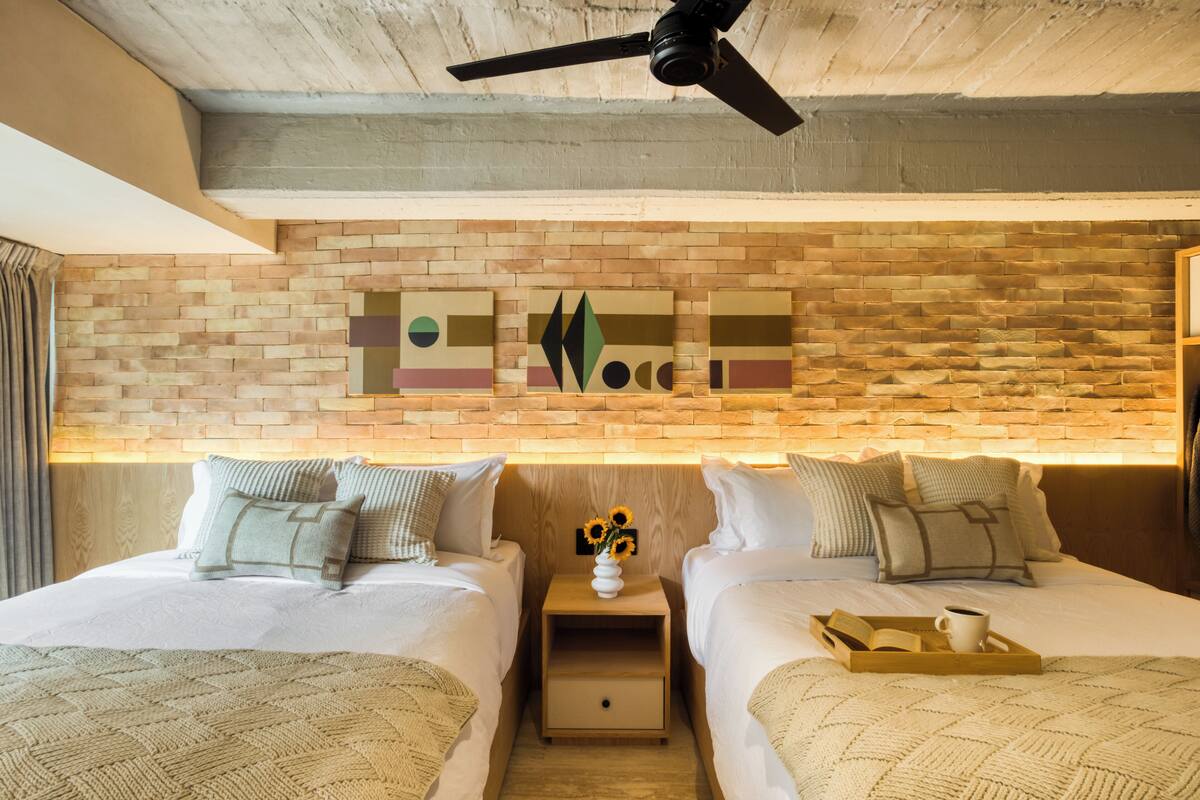 A hotel room with two beds, a nightstand with a vase of sunflowers, and a tray with a book and a cup.