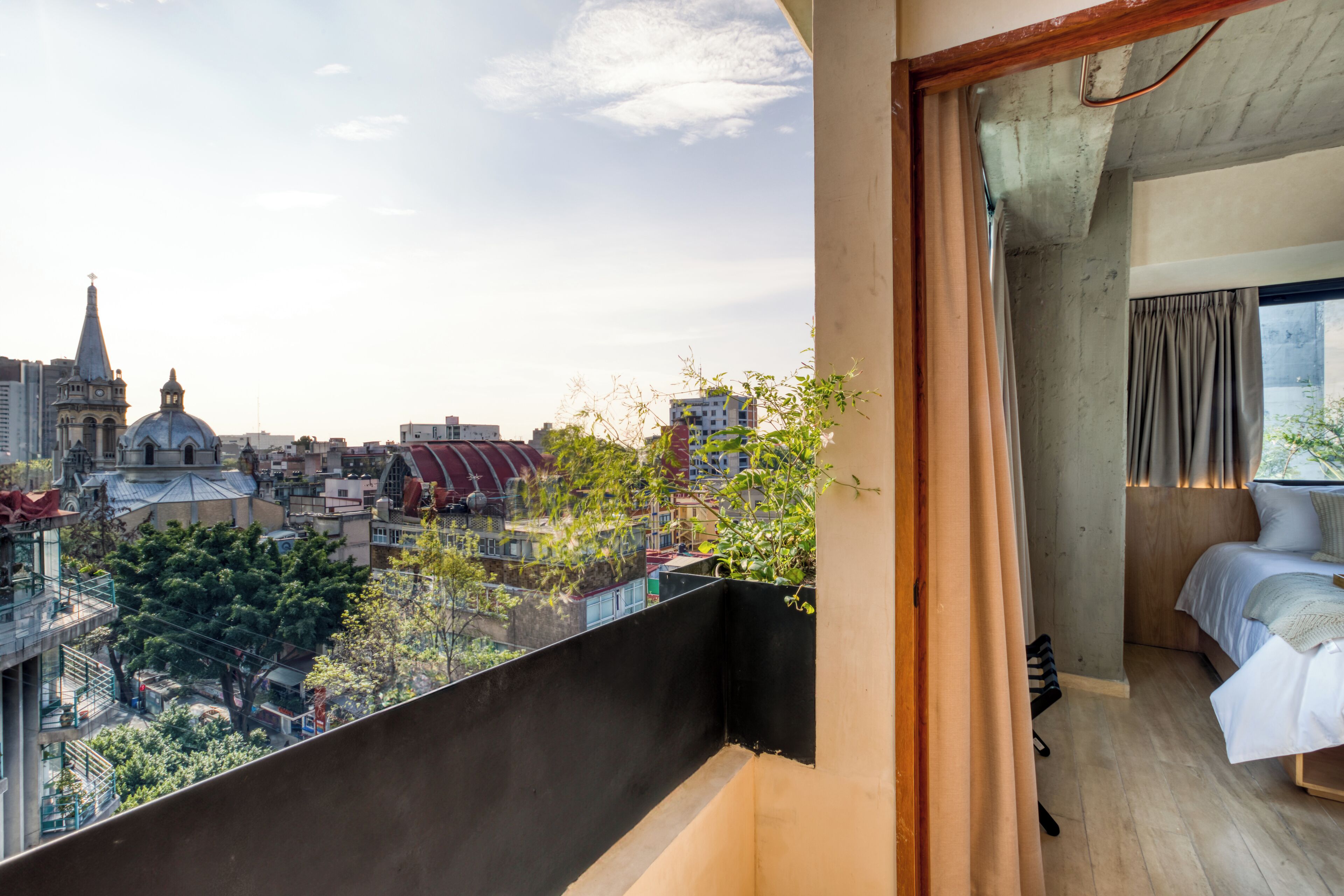 A room with a bed, a window, and a view of a cityscape including a church and buildings.