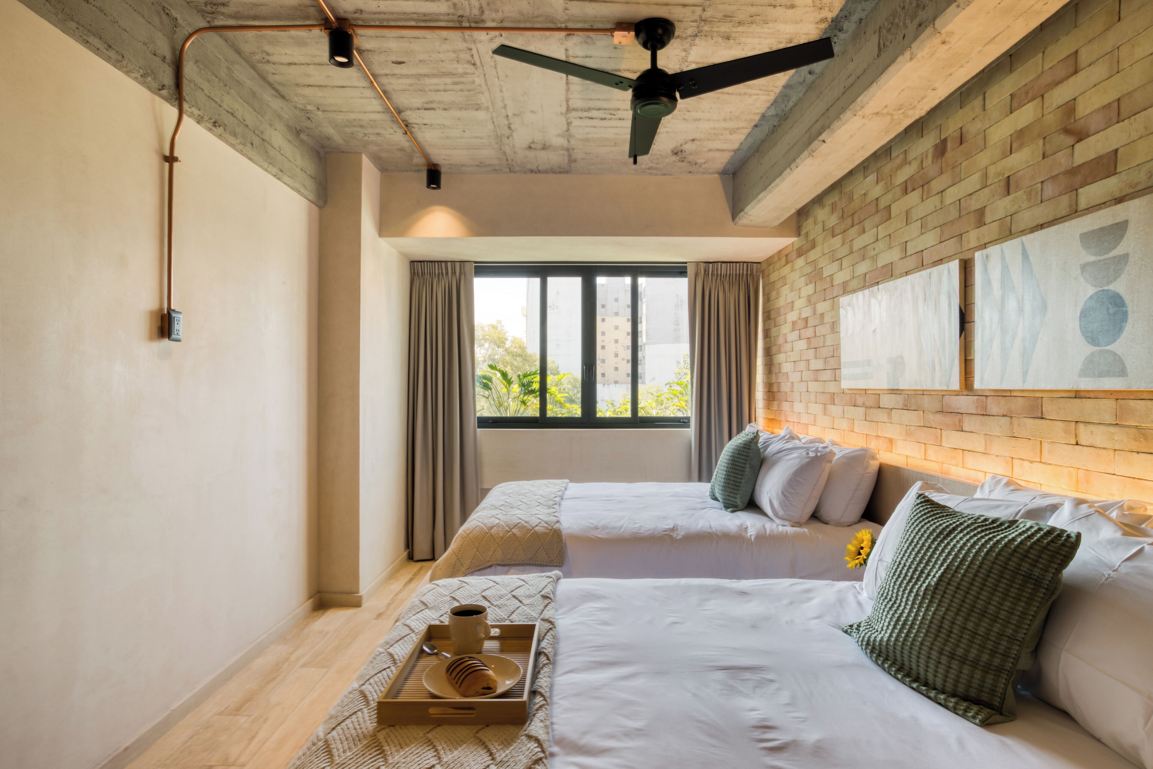 A modern hotel room with two beds, a ceiling fan, and a large window with curtains.