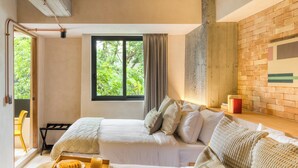 A bedroom with two beds, a window with a view of greenery, a brick wall, and a wooden shelf with a red object. - Caliza Roma Residences by Tasman (Mexico City)