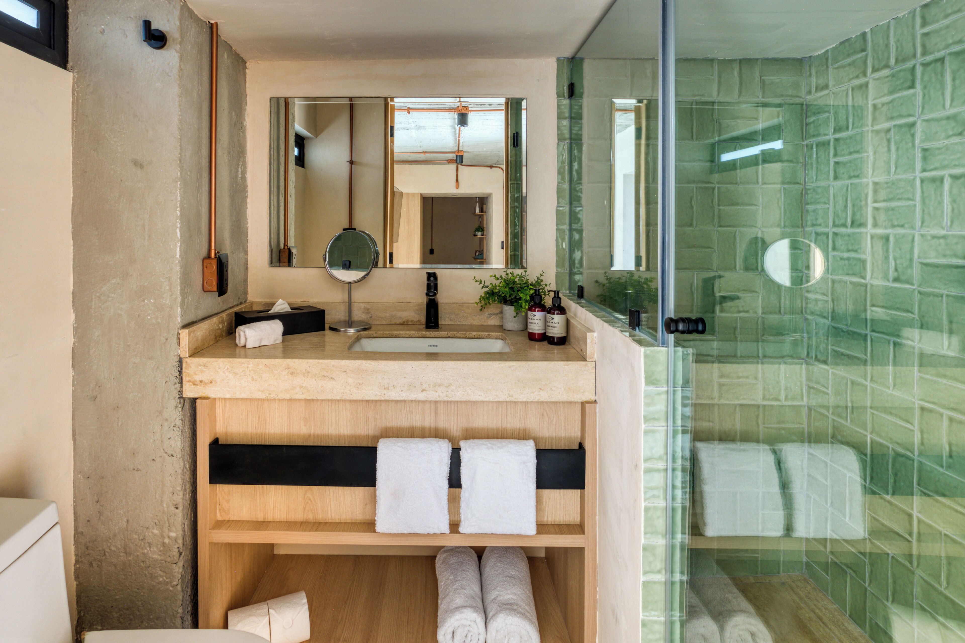 Ein Badezimmer mit einem Holztisch, einem Spiegel, einem Waschbecken und einer Duschkabine aus Glas mit grünen Fliesen.