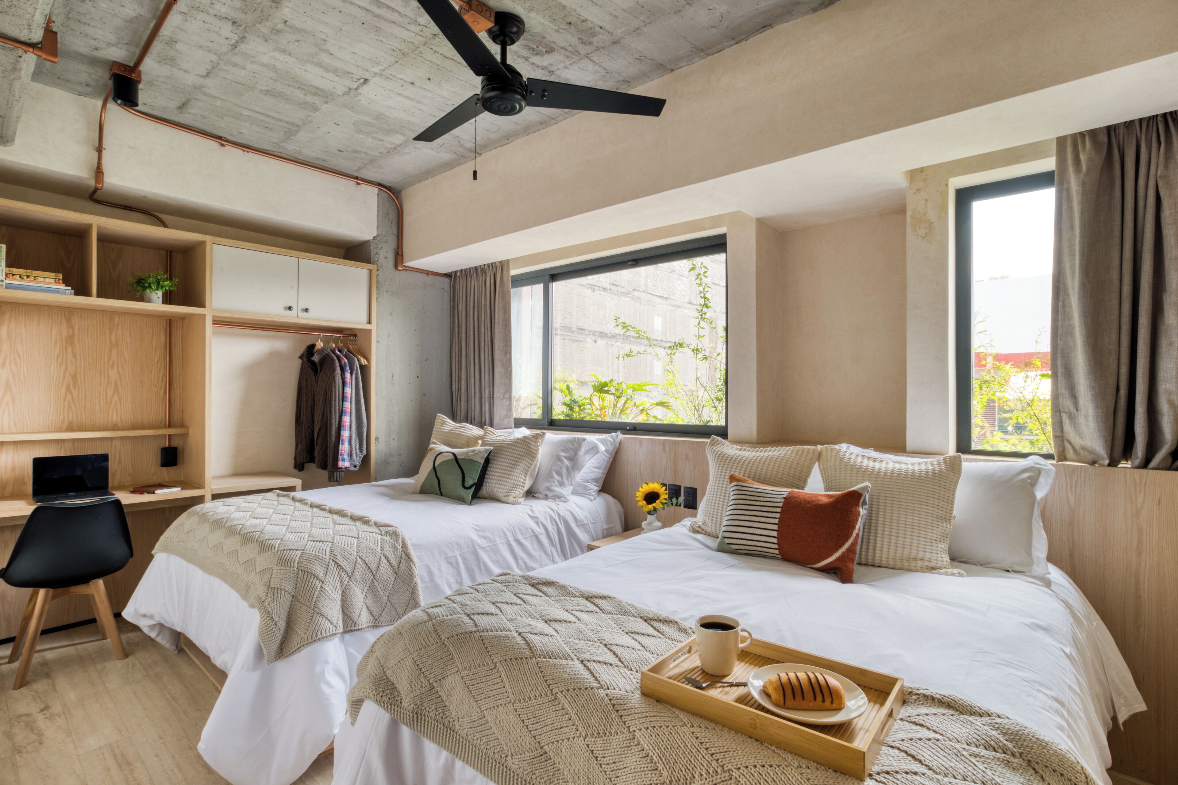 Une chambre moderne avec deux lits, un bureau et un ventilateur de plafond.