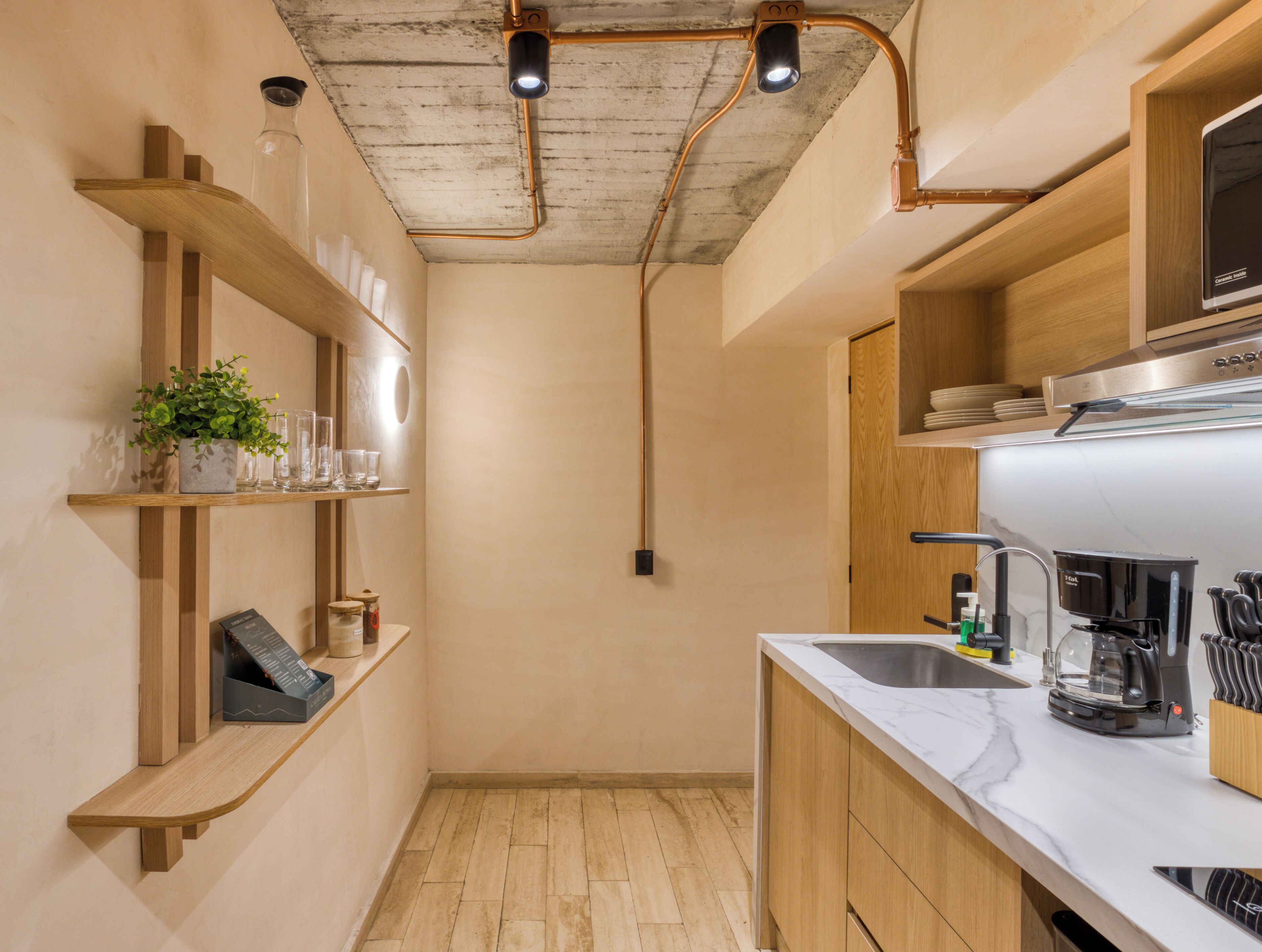 Una cocina compacta con estantes de madera, un lavamanos y electrodomésticos modernos.