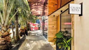 A corridor with a wooden ceiling, palm trees, and a sign for 'Caliza Roma'. - Caliza Roma Residences by Tasman (Mexico City)