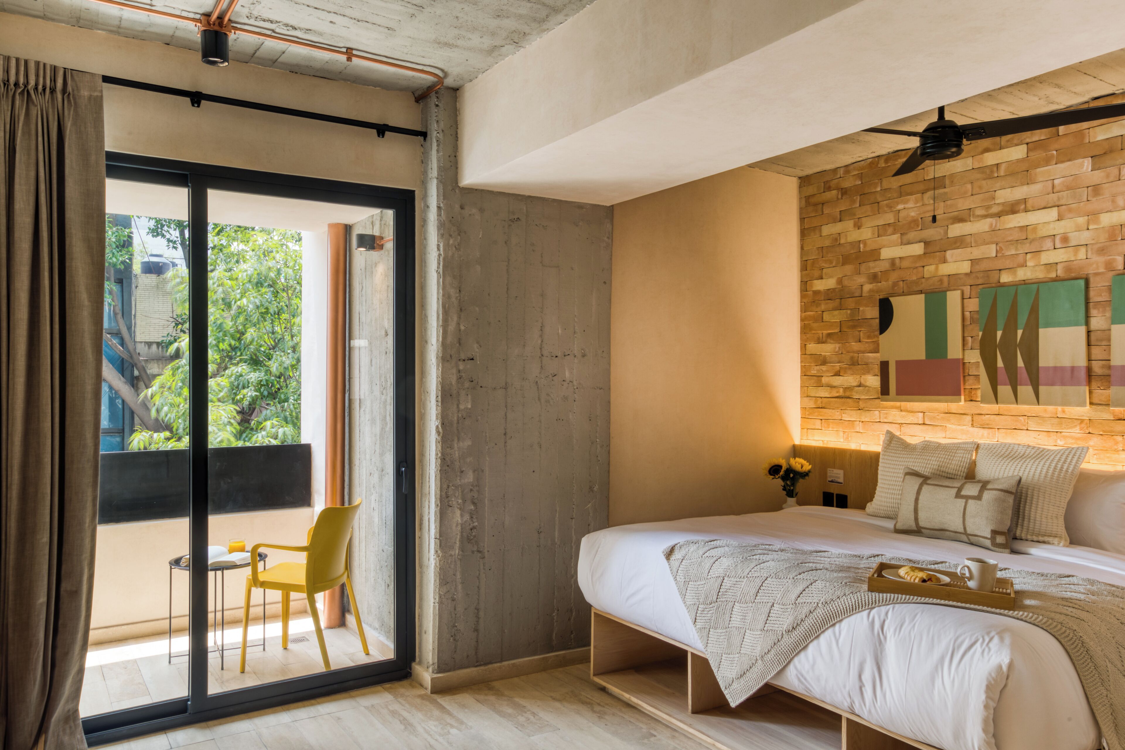 A bedroom with a bed, a chair, a table, and a view through a sliding door.