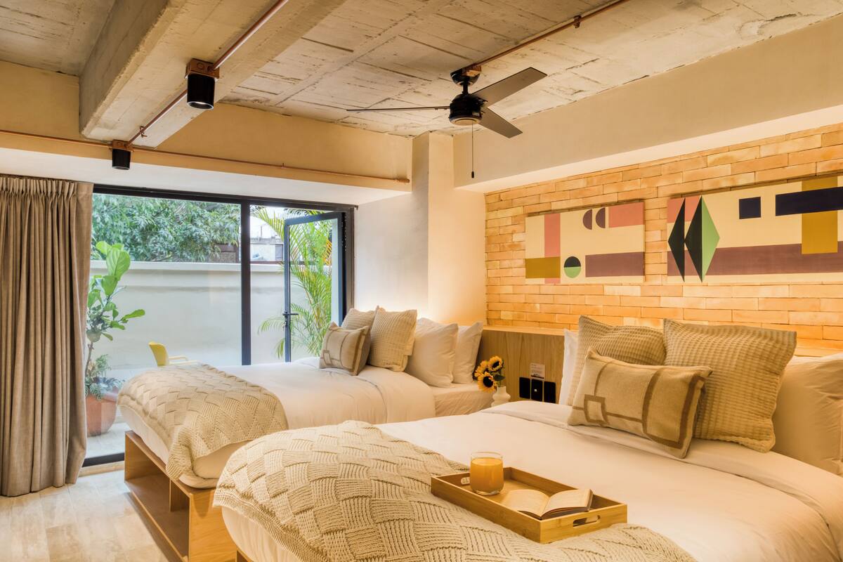 A modern hotel room with two beds, a brick accent wall, and a large window with curtains.
