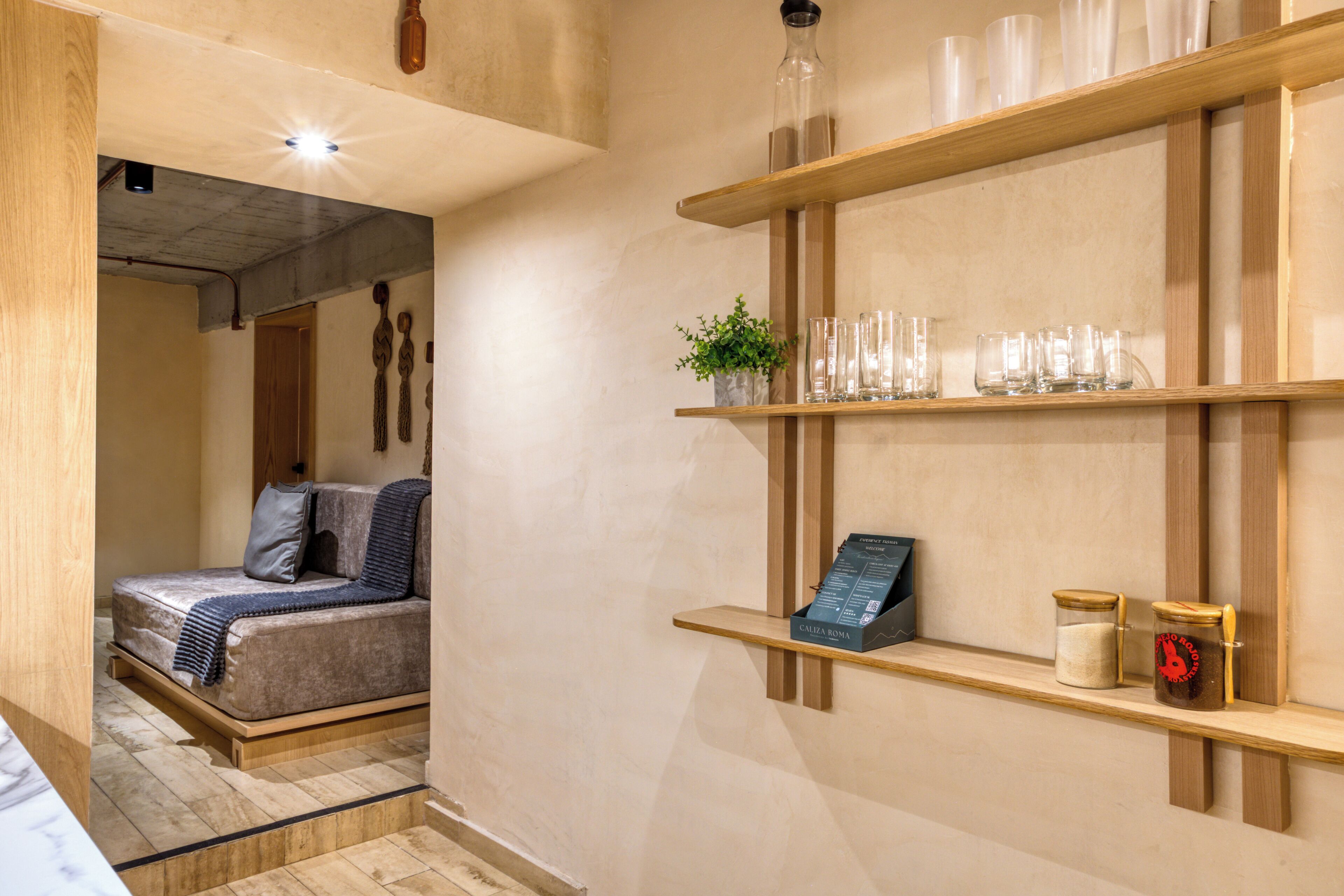 Une chambre d’hôtel avec un lit en bois, un petit coin salon et une étagère où sont posés des verres et une plante.